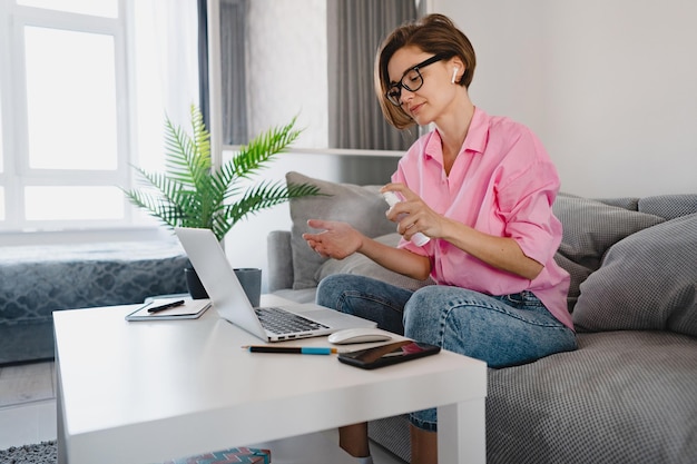 Vrouw spray ontsmettingsmiddel antiseptisch op handen op de werkplek thuis online werken op laptop