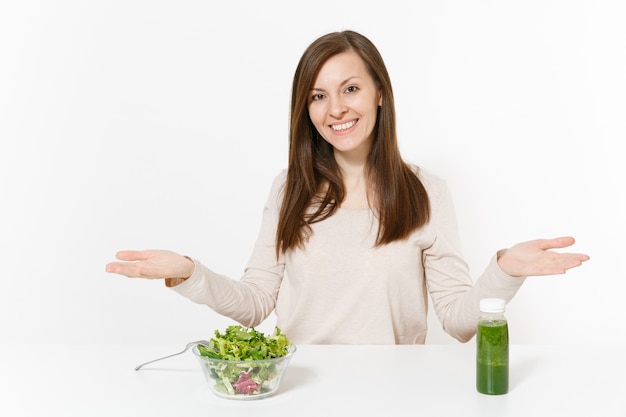 Vrouw spreidde handen aan tafel met groene detox smoothies, salade in glazen kom geïsoleerd op een witte achtergrond. Goede voeding, vegetarisch eten, gezonde levensstijl, dieetconcept. Gebied met kopie ruimte.