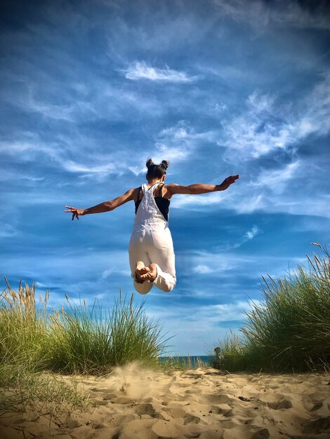Vrouw springt op zand tegen de lucht