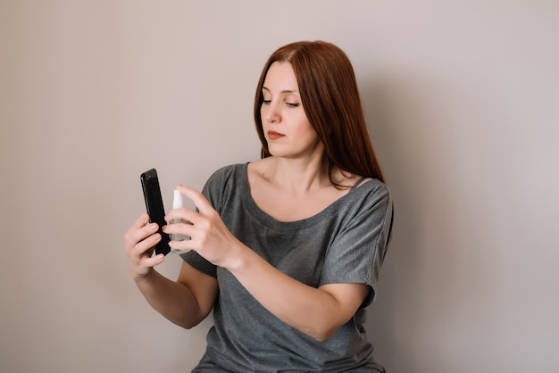 Vrouw spuit alcohol desinfecterende spray op smartphone