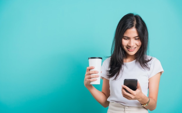 Vrouw staande glimlach met behulp van mobiele telefoon haar koffiekopje vasthouden