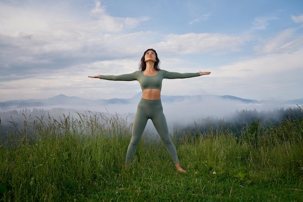 Vrouw staande op gras op bergheuvel in pose van winnaar