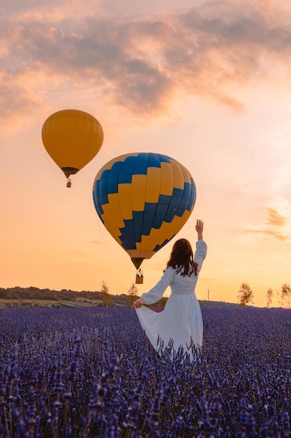 Vrouw staande op lavendelveld kijken naar luchtballonnen met mand zonsondergang tijd