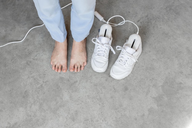 Vrouw staat blootsvoets in de buurt van witte schoenen die drogen met elektrische droger