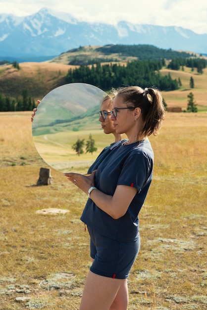 Vrouw staat in de zomer altai bergen in Kurai steppe en houdt cirkelspiegel creatieve reis vast...