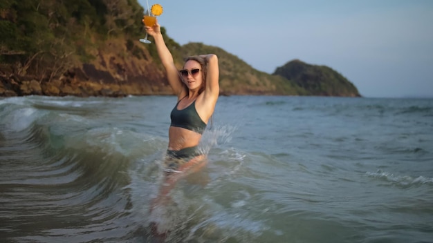 Vrouw staat kniediep in zee bij zonsondergang Meisje op strand in groene s