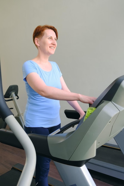 Vrouw staat op een loopband in de sportschool en glimlacht