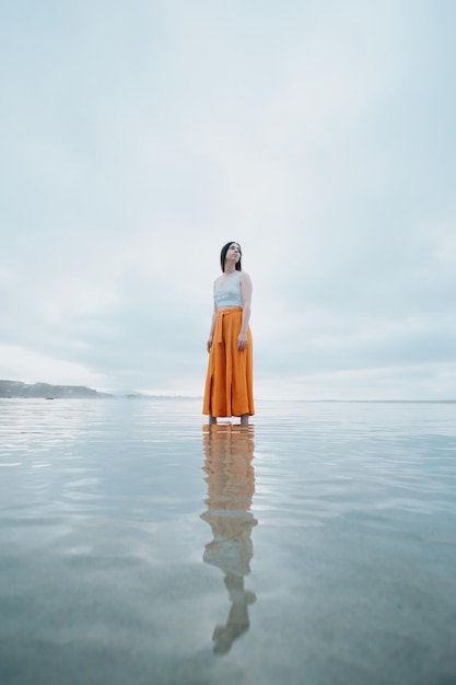 Vrouw staat op trendy kleding op het strand terwijl ze nadenkt over het water