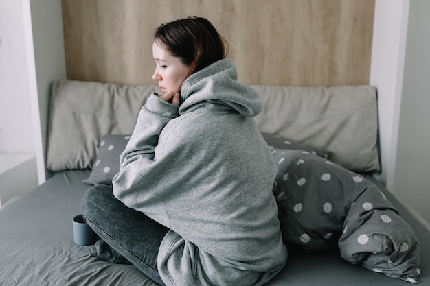 Vrouw staat 's ochtends vroeg op en drinkt koffie in een gezellige slaapkamer thuis en wordt wakker met rust