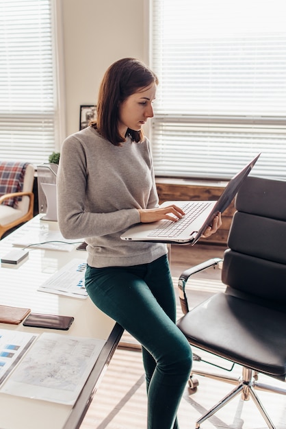 Vrouw staat te typen op het toetsenbord van een notebook in haar kantoor