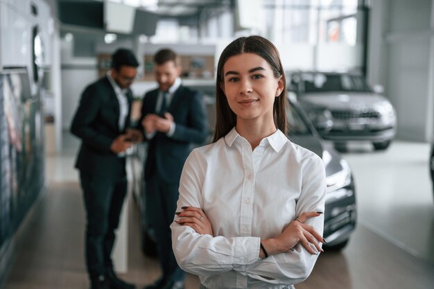 Vrouw staat voor haar collega's Drie mensen werken samen in de autoshowroom