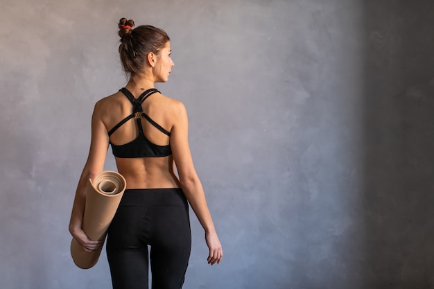 Vrouw stond op het werk of yogales met opgerolde fitness mat in haar hads draaide haar terug naar de camera. Kopieer ruimte op een donkere achtergrond