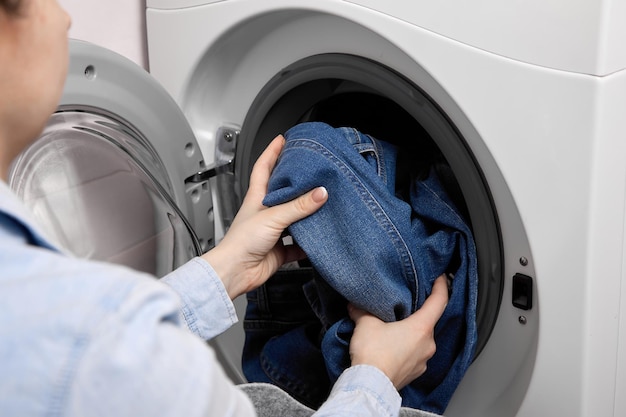 Vrouw stopt vuile spijkerbroek in de trommel van een wasmachine om te wassen