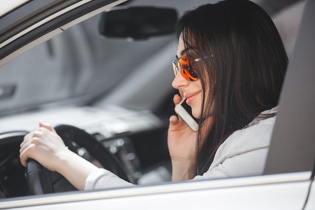 Vrouw stuurprogramma praten over telefoon. Mooi meisje in de auto. Lady besturen van een witte auto.