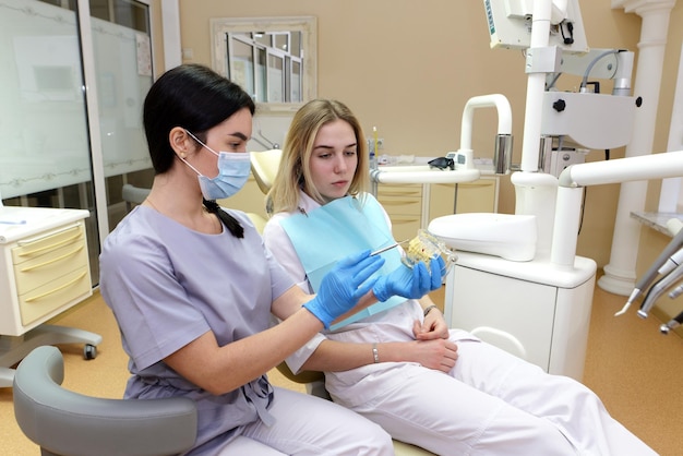 Vrouw tandarts die op een kaakmodel laat zien hoe de tanden met een tandenborstel goed moeten worden schoongemaakt en het juiste geduldige meisje hoorde de dokter