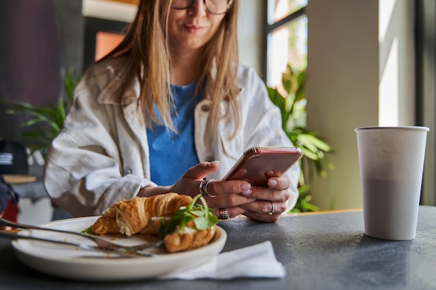 Vrouw tekstbericht aan het typen op smartphone in een café Bijgesneden afbeelding van jonge vrouw zittend aan een tafel met een kopje koffie met mobiele telefoon Toned Selective focus