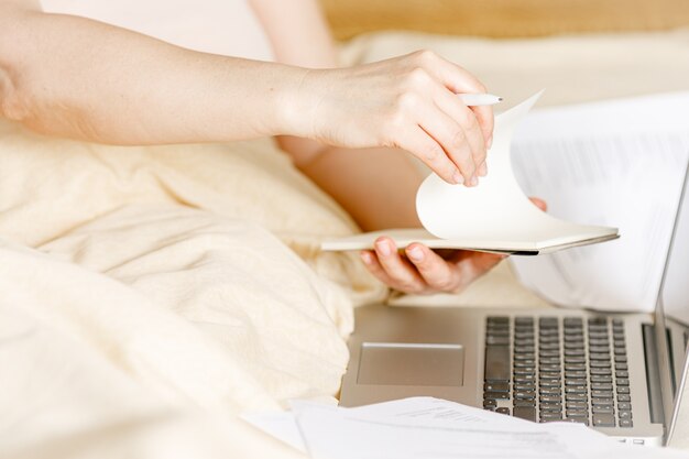 Vrouw telewerken van het bed met laptop en documenten, freelancer concept