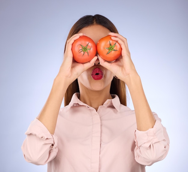 Vrouw tomaat en bedekkende ogen in studio voor gezonde voeding veganistisch dieet en groente in handen Gezicht van een model persoon met rode groenten voor gezondheid, wellness en huidverzorging op paarse achtergrond