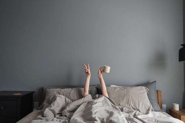 Vrouw tot in bed, mok met koffie in de hand te houden en te laten zien