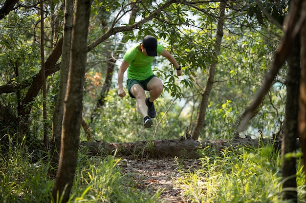 Vrouw trail runner rennen en springen over een omgevallen boomstam in tropisch bos berg