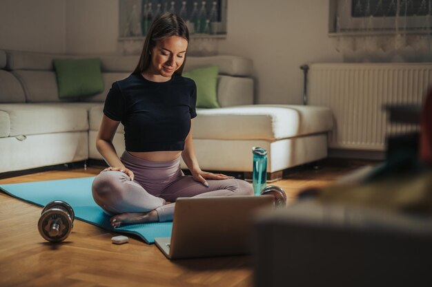 Vrouw traint thuis terwijl ze een laptop en airpods gebruikt voor haar online training