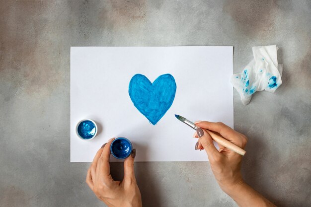 Vrouw trekt een hart met blauwe verf. creatie. Onderwijs in schilderen.