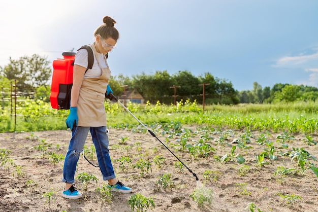 Vrouw tuinman met drukspuit rugzak spuiten jonge tomatenplanten in de lente moestuin beschermen tegen bacteriële ziekten plaagparasieten chemische en biologische preparaten