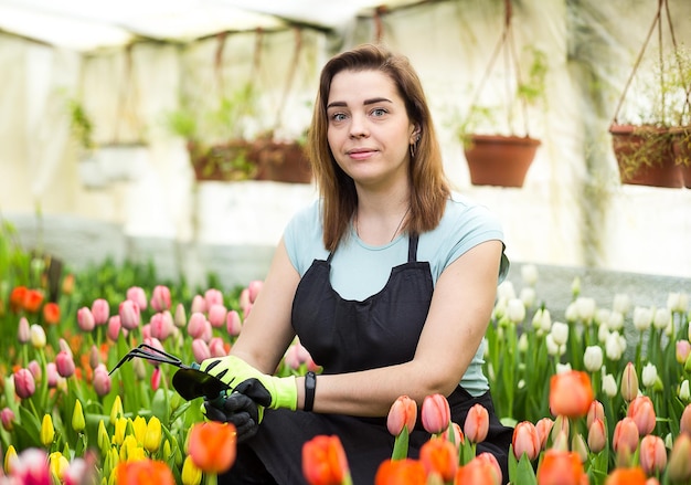 Vrouw tuinman met tuingereedschap in de kasBloemistenvrouw die met bloemen in een kas werkt Lente veel tulpenbloemen conceptIndustriële teelt van bloemen