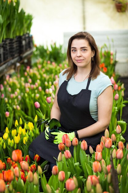 Vrouw tuinman met tuingereedschap in de kasBloemistenvrouw die met bloemen in een kas werkt Lente veel tulpenbloemen conceptIndustriële teelt van bloemen