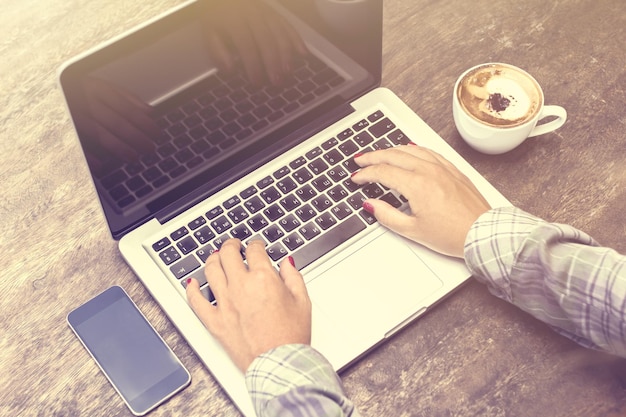 Vrouw typen op een laptop met mobiele telefoon en koffie