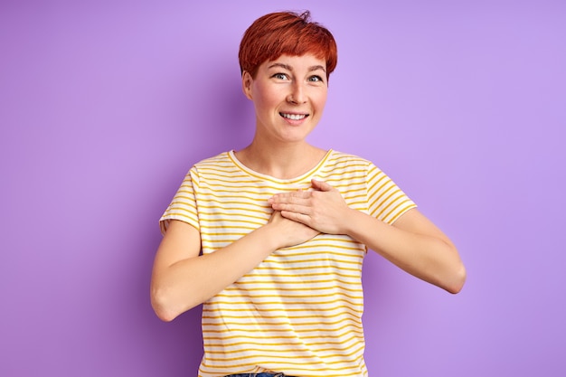 Vrouw uiting van dankbaarheid, hand in hand op de borst, vriendelijkheid voelen. geïsoleerd over paarse muur