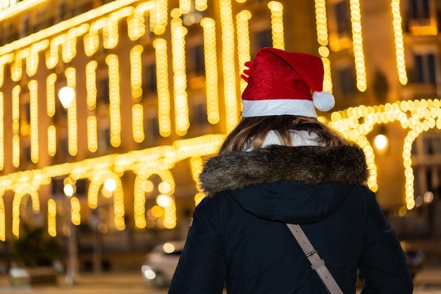 Vrouw van achteren met kerstmuts in het verlichte gebouw van de nachtstad