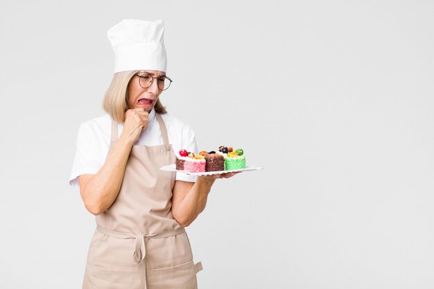 Vrouw van de middelbare leeftijd de mooie bakker met cakes tegen exemplaar ruimtemuur