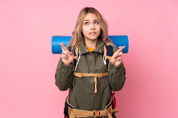 Vrouw van de tiener de Russische bergbeklimmer met een grote die rugzak op roze muur wordt geïsoleerd met vingers die kruisen en het beste wensen