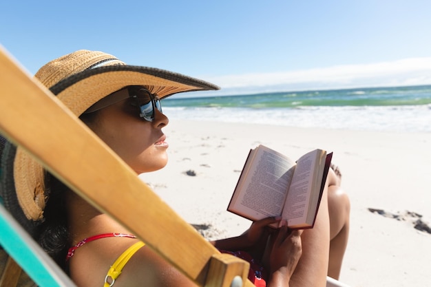 Vrouw van gemengd ras op strandvakantie zittend in ligstoel leesboek. gezonde vrije tijd buitenshuis aan zee.