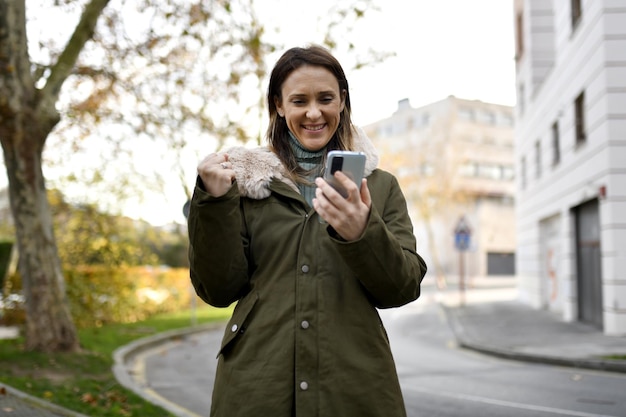 Foto vrouw van middelbare leeftijd beschut tegen de kou in de winter kijkend naar de smartphone terwijl ze haar vuist viert