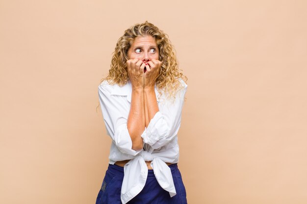 Vrouw van middelbare leeftijd die bezorgd, angstig, gestrest en bang kijkt, vingernagels bijt en naar laterale kopieerruimte kijkt