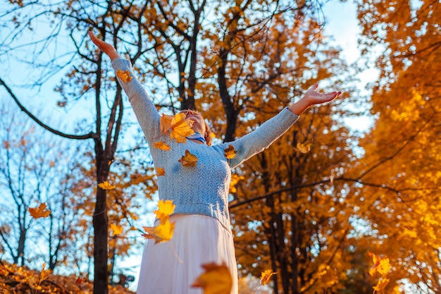 Vrouw van middelbare leeftijd die bladeren in de herfstbos werpt Hogere vrouw die pret heeft