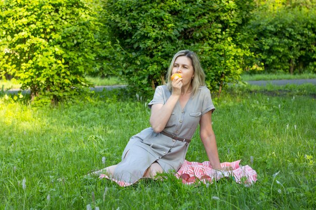 Vrouw van middelbare leeftijd die een appel eet op het grasveld in het park