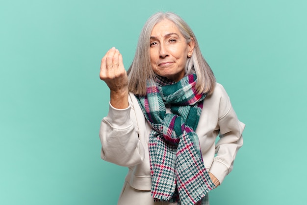 Vrouw van middelbare leeftijd die een capice of geldgebaar maakt en u vertelt uw schulden te betalen!