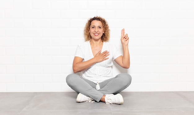 Foto vrouw van middelbare leeftijd die er gelukkig, zelfverzekerd en betrouwbaar uitziet, glimlacht en een overwinningsteken toont, met een positieve instelling