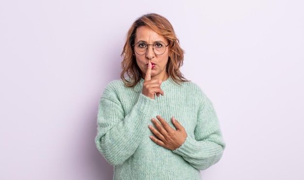 Vrouw van middelbare leeftijd die er serieus uitziet en kruist met de vinger tegen de lippen gedrukt die stilte of stilte eist en een geheim bewaart