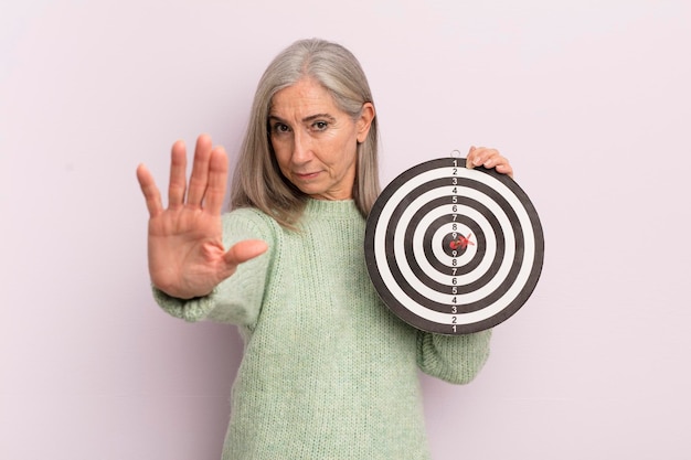 Vrouw van middelbare leeftijd die er serieus uitziet en open palm laat zien die stopgebaar darts doelconcept maakt