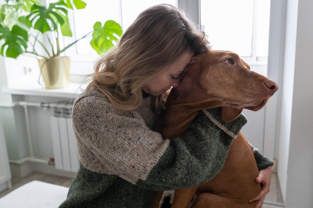 Vrouw van middelbare leeftijd die haar geliefde ruwharige vizsla-hond knuffelt bij het concept van de dierentherapie thuis