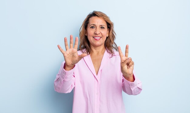 Vrouw van middelbare leeftijd die lacht en er vriendelijk uitziet, nummer zeven of zevende toont met de hand naar voren, aftellend