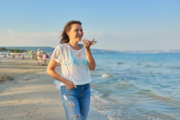 Vrouw van middelbare leeftijd die langs het strand loopt met smartphone