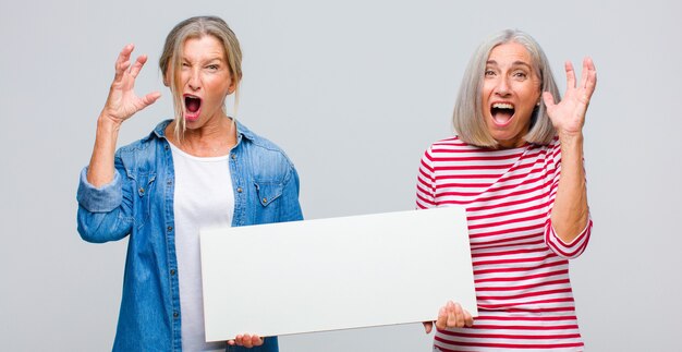 Vrouw van middelbare leeftijd die met handen in de lucht schreeuwt, zich woedend, gefrustreerd, gestrest en boos voelt