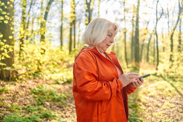Vrouw van middelbare leeftijd die mobiele telefoon in handen houdt buitenshuis mooie rijpe vrouw in groen sportief wij