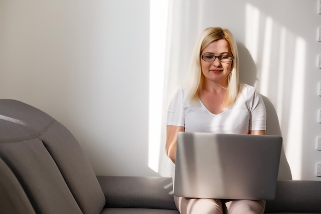 Vrouw van middelbare leeftijd die thuis op laptop werkt