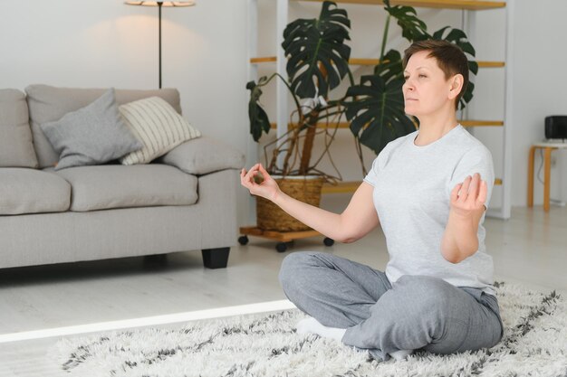 Vrouw van middelbare leeftijd die thuis yoga doet om uit te rekken en gezond te zijn